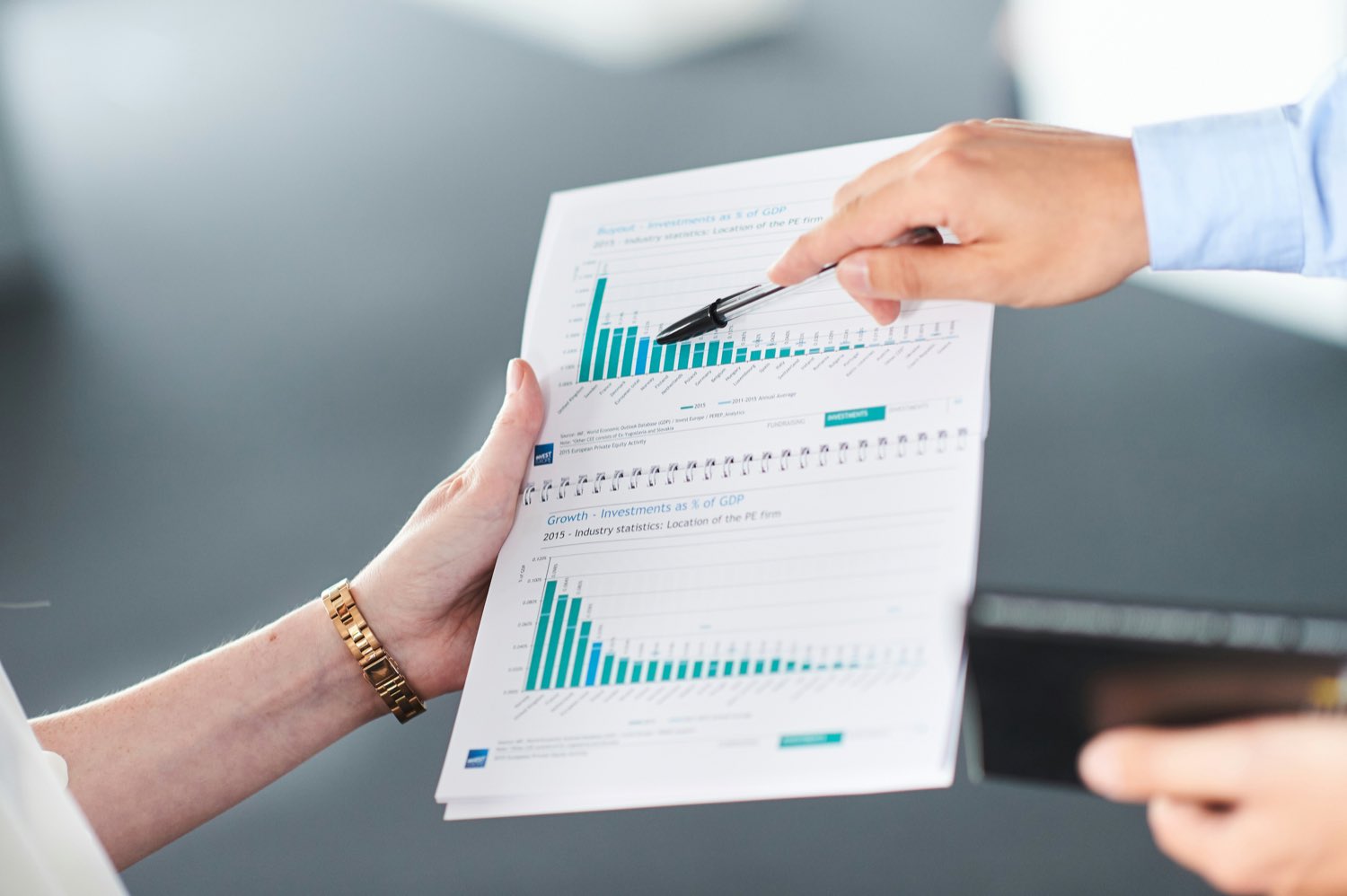 A printed bar chart held open and pointed at across a table