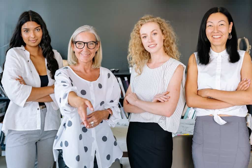 Smiling diverse group of businesswomen, arms crossed, in modern office setting.